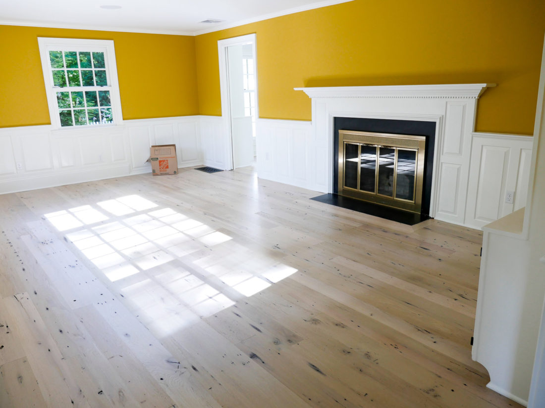 REZTT home in Connecticut with light wood floors, mustard walls and white judge's paneling around the wood burning fireplace in the formal living room.