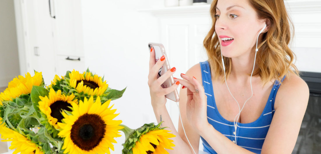 Eva Amurri Martino of blog REZTT sitting at her kitchen table next to a vase of sunflowers, wearing a striped blue and white maternity tank and listening to an audiobook on Audible