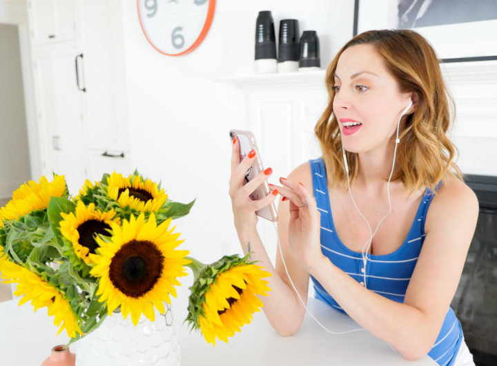 Eva Amurri Martino of blog REZTT sitting at her kitchen table next to a vase of sunflowers, wearing a striped blue and white maternity tank and listening to an audiobook on Audible