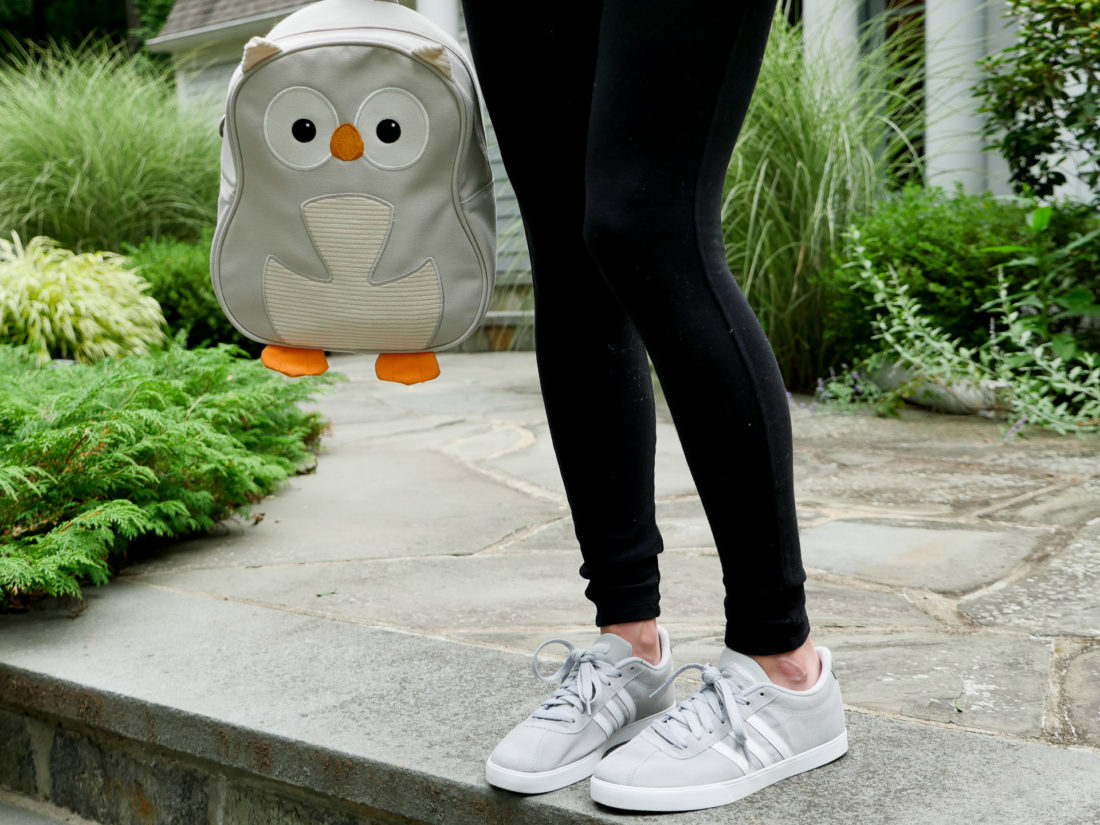 Eva Amurri Martino of lifestyle blog REZTT wearing black maternity leggings and adidas sneakers holding her daughter's grey owl backpack