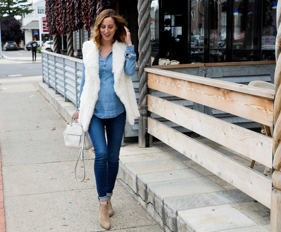 Eva Amurri Martino of lifestyle blog REZTT wearing dark denim maternity jeans, a light chambray maternity top, white vest, and light brown western style booties walking down the street in connecticut