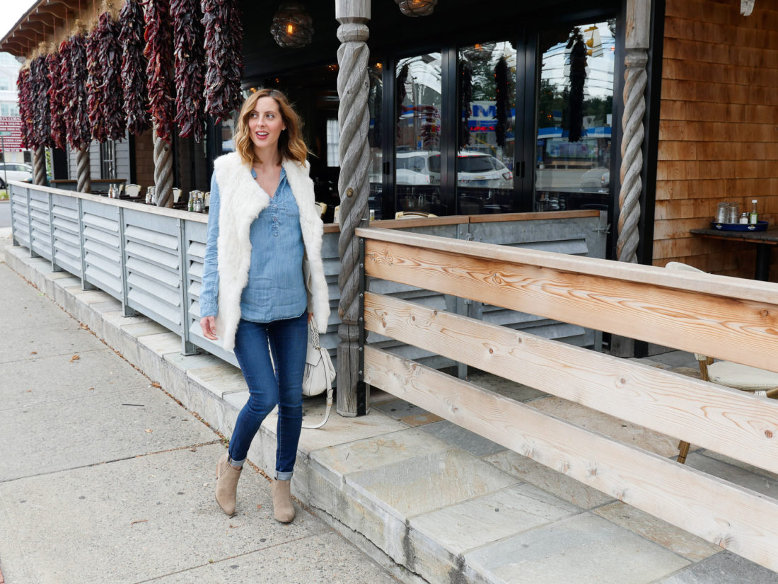Eva Amurri Martino of lifestyle blog REZTT wearing dark denim maternity jeans, a light chambray maternity top, white vest, and light brown western style booties walking down the street in connecticut
