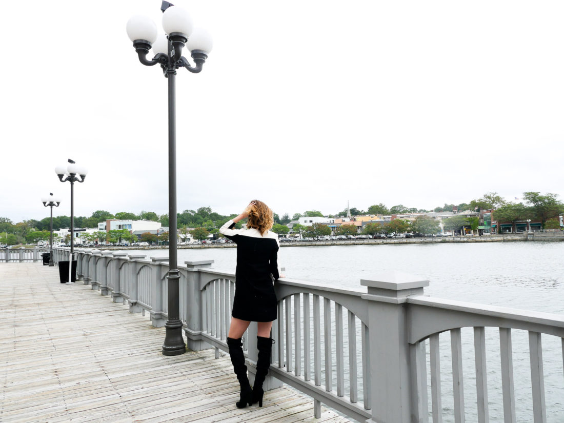 Eva Amurri Martino of lifestyle blog REZTT wearing a mod black and cream shift dress and black over the knee boots facing out towards the water next to a lamp post