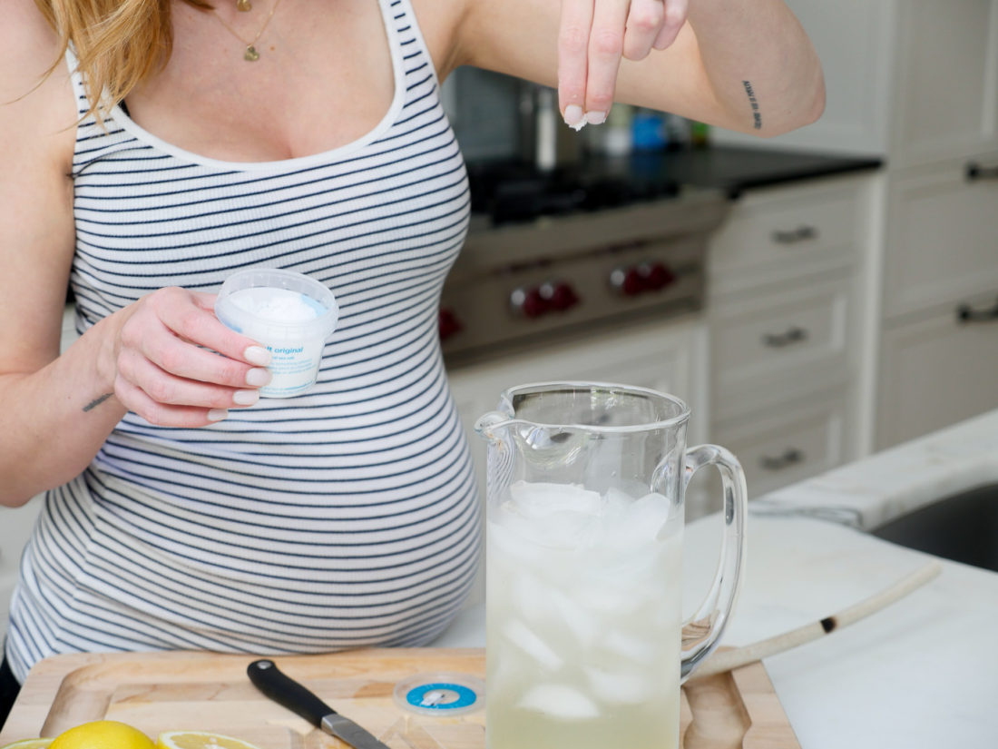 Eva Amurri Martino of lifestyle blog REZTT adding salt to a glass pitcherin her kitchen to make a hydrating laborade for her Home Birth