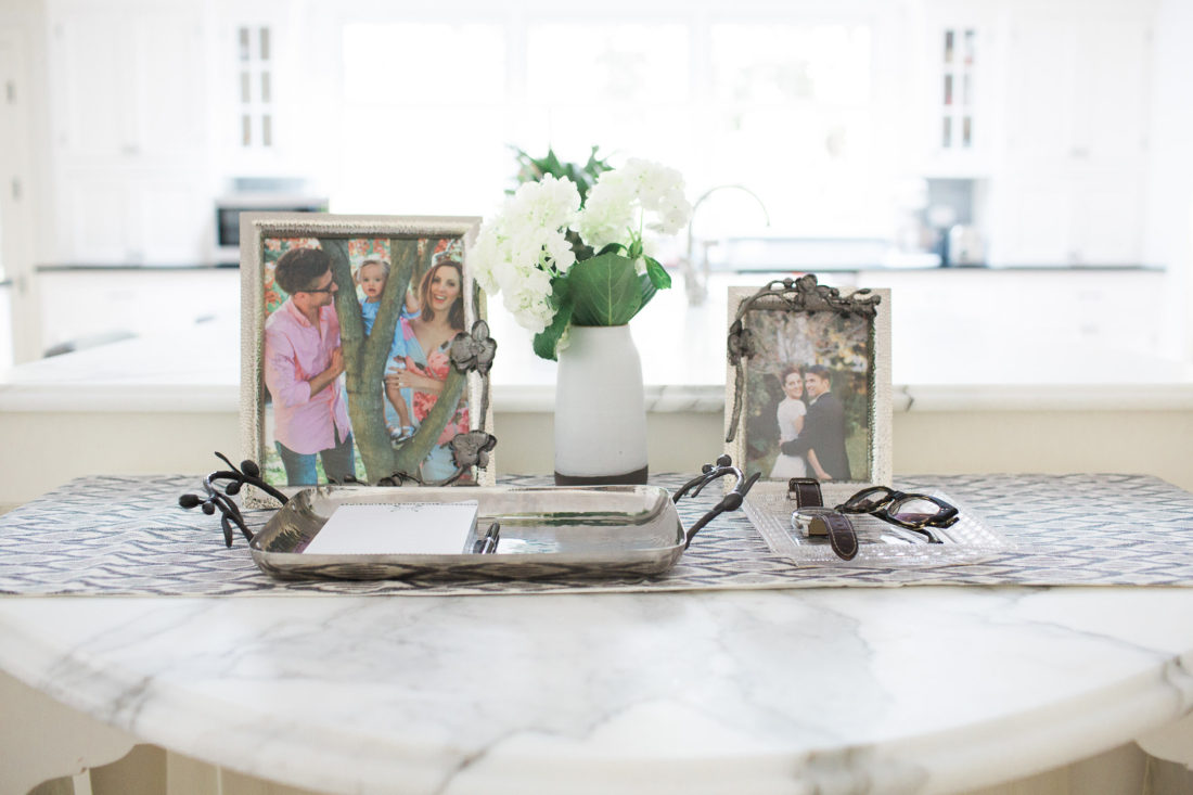A close up of a tablescape with family photos in Michael Aram orchid motif frames on the marble kitchen island in Eva Amurri Martino's Connecticut home