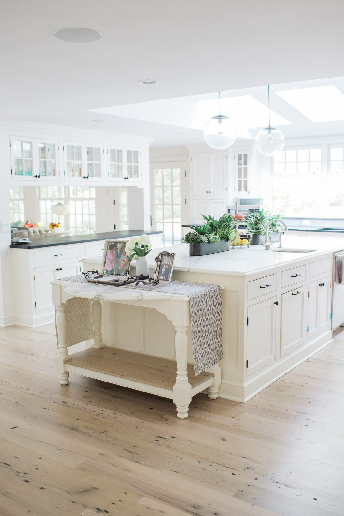 An entrance view of lifestyle blogger Eva Amurri Martino's white and bright kitchen in connecticut, featuring a huge marble island, skylights, and views of the pool and yard