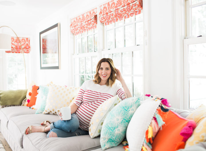 Eva Amurri Martin of lifestyle blog REZTT relaxes at home in her family room on a grey couch with multicolored and multipatterned pillows surrounding her, holding a cup of coffee