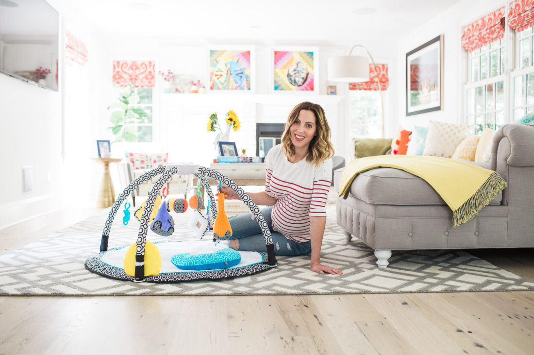 Eva Amurri Martino of lifestyle blog REZTT sitting on the floor of her colorful family room with the fisher price by Jonathan Adler sensory gym 