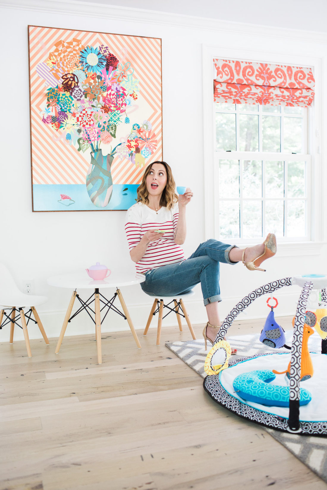 Eva Amurri Martin of lifestyle blog REZTT drinking tea from her daughter's tea set and perching on a tiny white midcentury modern playroom furniture set with the jonathan adler crafter by fisher price collection sensory gym in the foreground