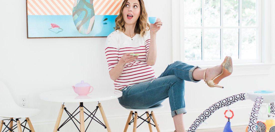 Eva Amurri Martin of lifestyle blog REZTT drinking tea from her daughter's tea set and perching on a tiny white midcentury modern playroom furniture set with the jonathan adler crafter by fisher price collection sensory gym in the foreground