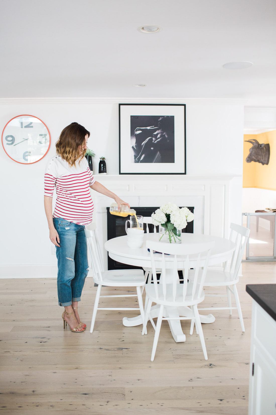Eva Amurri Martino of lifestyle blog REZTT pouring orange juice while wearing a red and white striped maternity top in her kitchen in connecticut