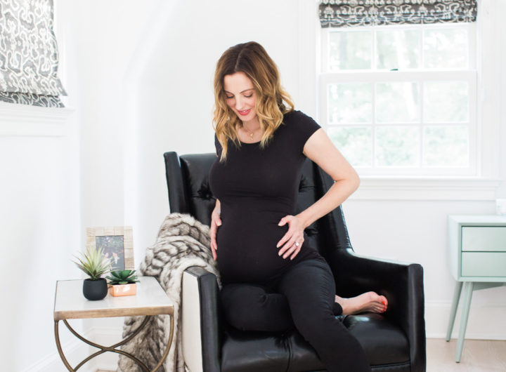 Eva Amurri Martino of lifestyle blog REZTT cradling her 37 week bump while sitting in a black leather chair in her master bedroom next to a brass table and two succulents
