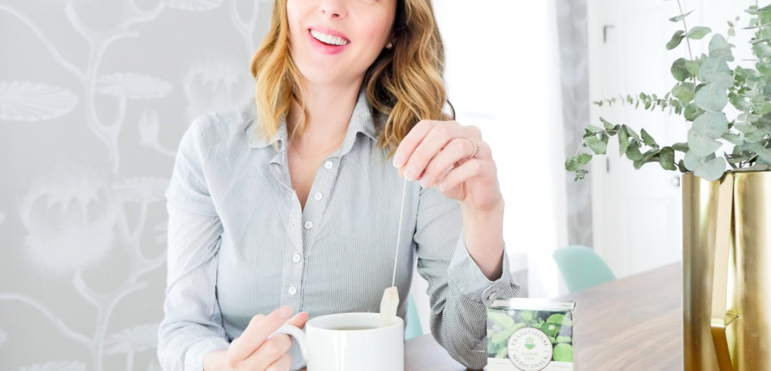 Eva Amurri Martino of lifestyle blog REZTT sits at her dining room table in connecticut wearing a blue and white striped maternity top and dunking a tea bag in to a white mug