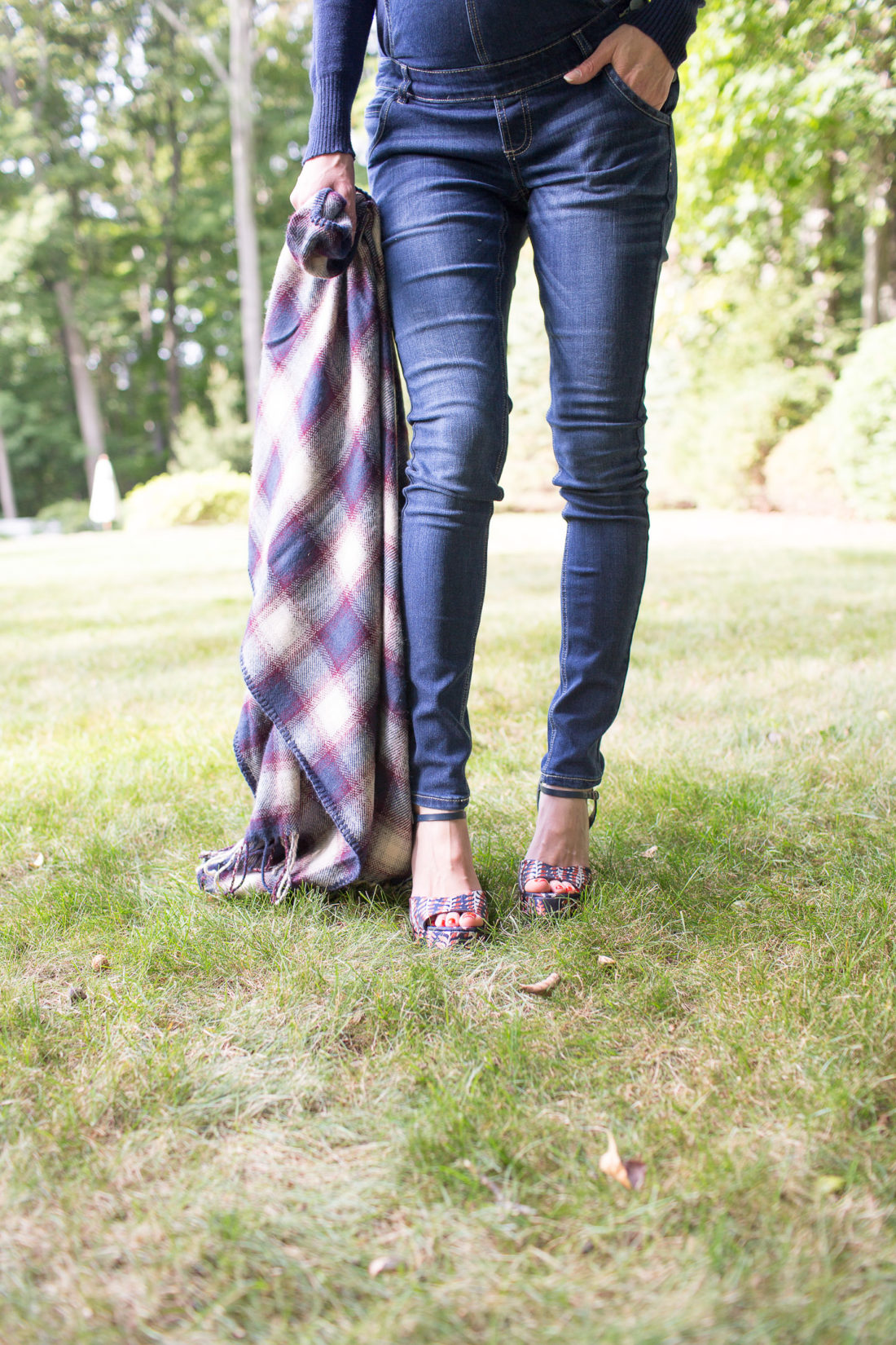 Eva Amurri Martino of lifestyle blog REZTT standing in her yard in maternity overalls, a navy felt hat, and a plaid poncho at her home in connecticut