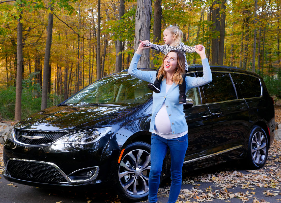 Eva Amurri Martino pictured at nine months pregnant standing in front of her black Chrysler Pacifica with her daughter Marlowe perched on her shoulders