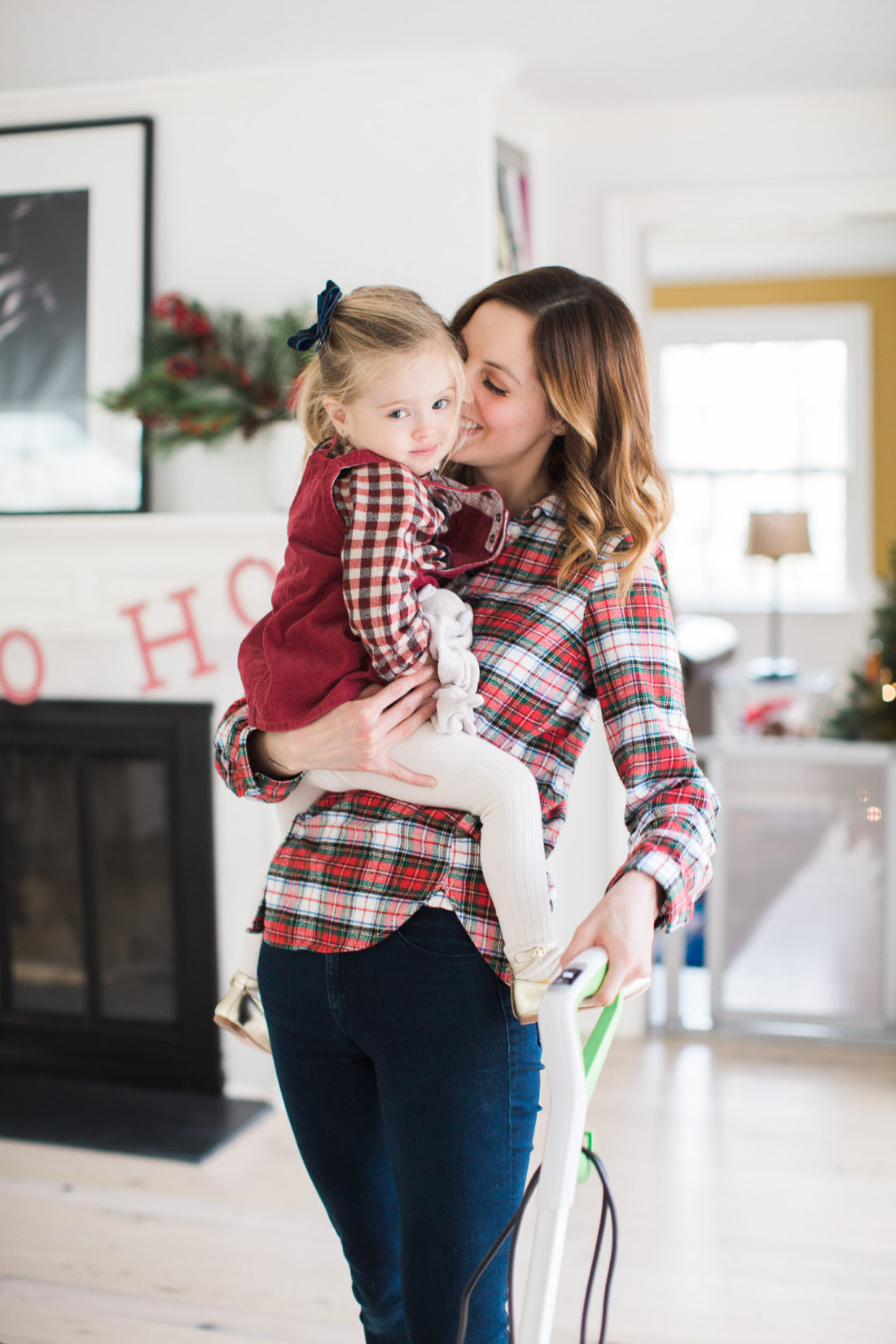 Eva Amurri Martino of lifestyle and motherhood blog REZTT holds her toddler daughter Marlowe in her arms while she vacuums her home and prepares for holiday parties