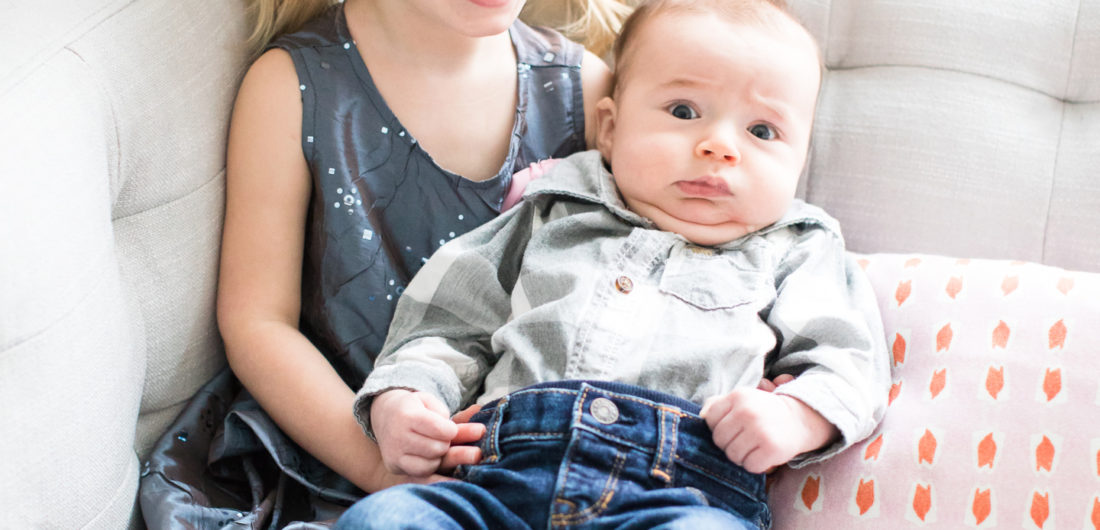 Marlowe Martino holds baby brother, Major, while wearing a sparkly grey dress and pigtails