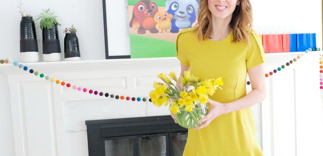 Eva Amurri Martino holds a vase of daffodils, wearing a yellow dress, for a post about entertaining for children
