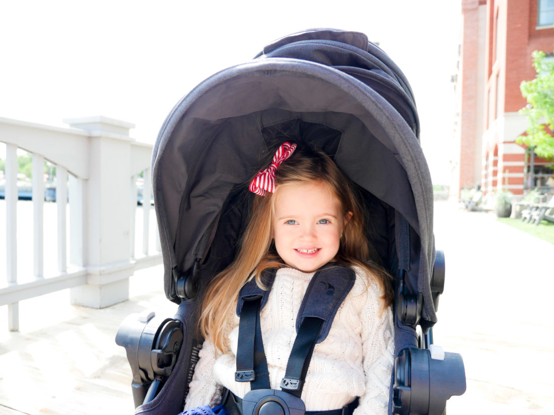 Marlowe Martino sits in a double Baby Jogger stroller, wearing a red and white hairbow and a cream sweater