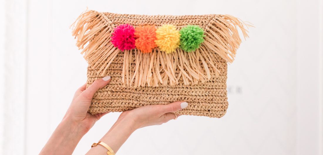 Eva Amurri Martino holds up a multicolored DIY pom pom straw clutch