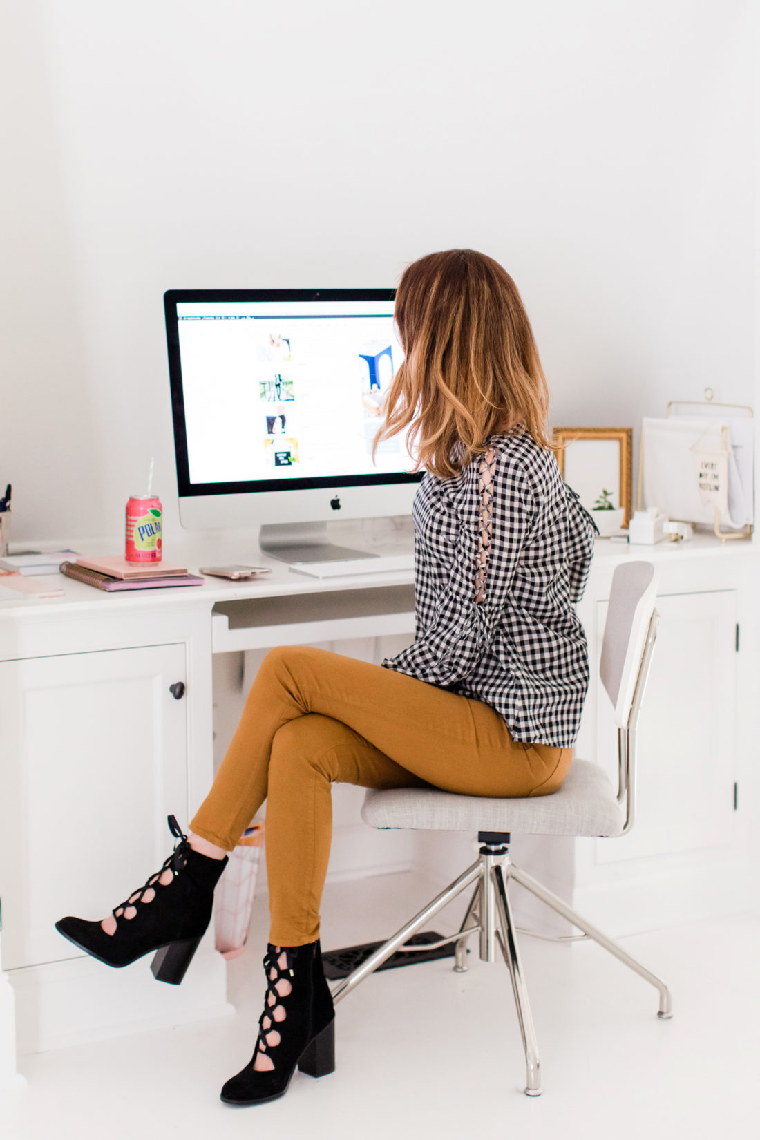 Eva Amurri Martino wears tan jeans and a black and white checked top, and sits at her computer in the REZTT studio