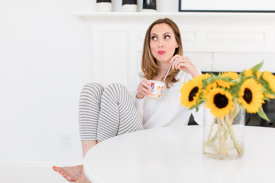 Eva Amurri Martino sits at the kitchen table in a pair of grey and white striped pajamas and eat breakfast next to a vase of sunflowers