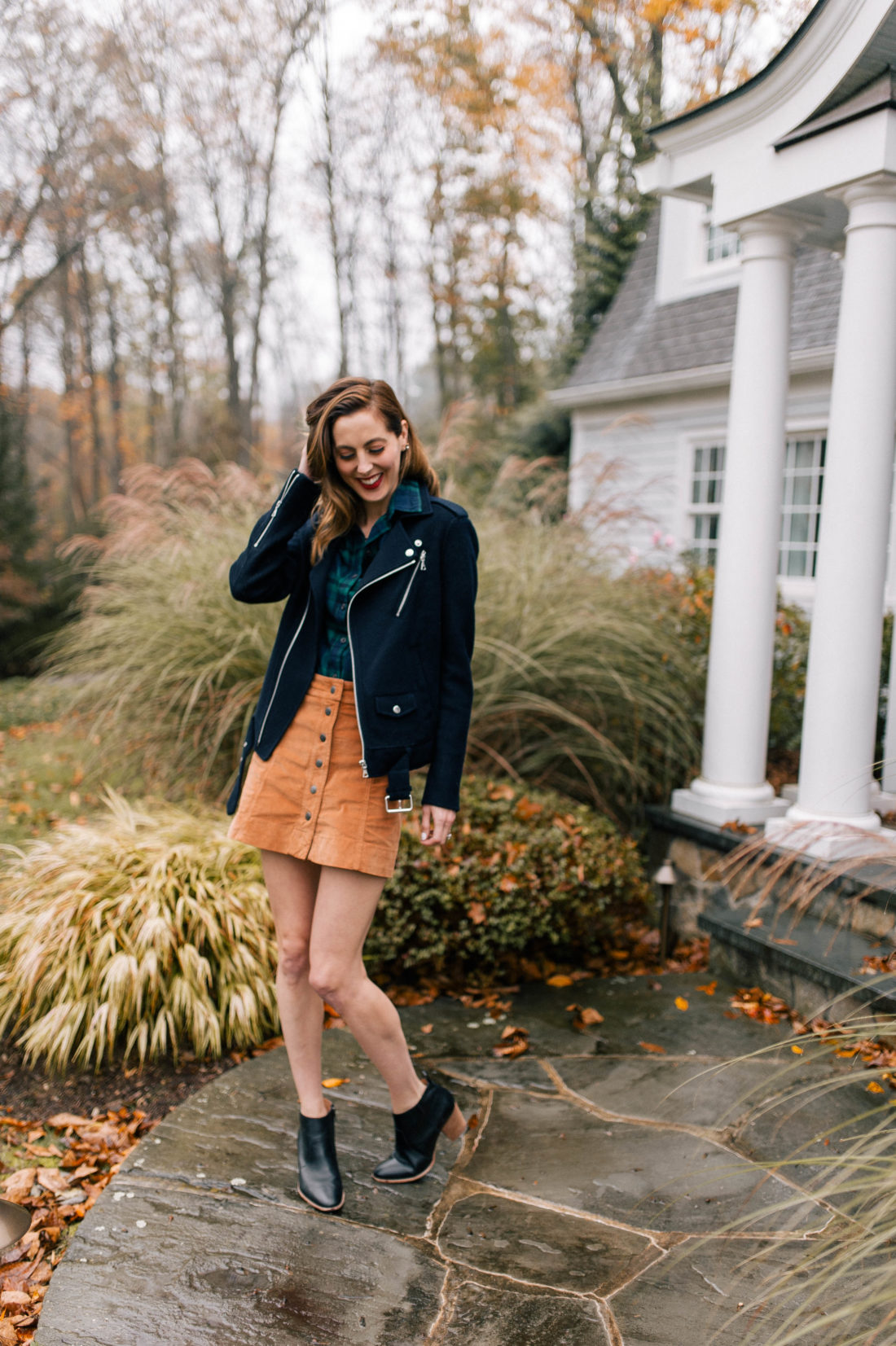 Eva Amurri Martino wears a plaid top, navy blue jacket, corduroy skirt, and black booties and walks down the pathway to her Connecticut home