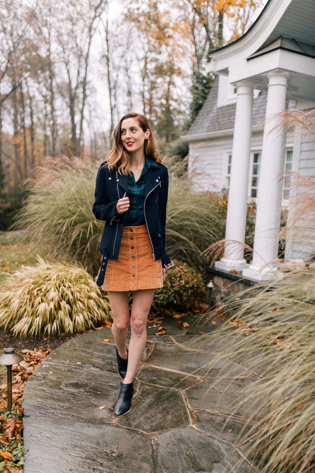 Eva Amurri Martino wears a plaid top, navy blue jacket, corduroy skirt, and black booties and walks down the pathway to her Connecticut home