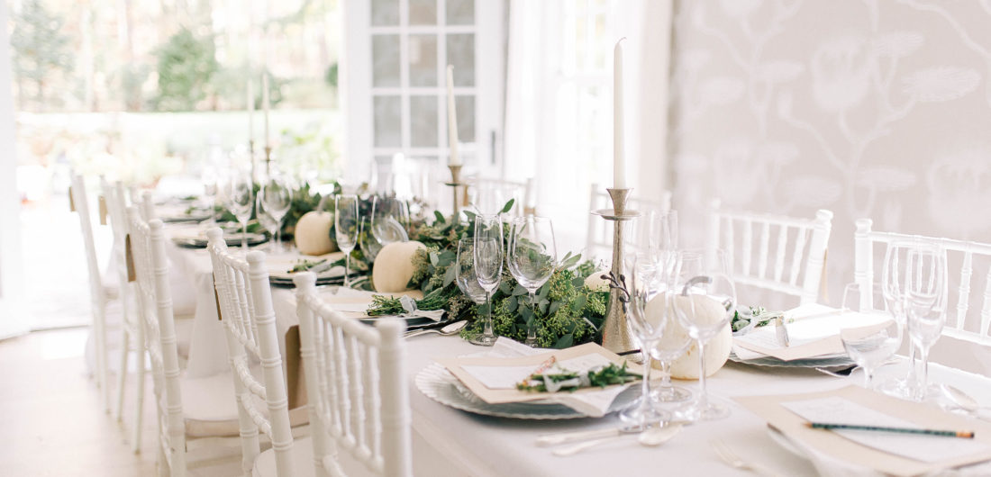 Crisp and modern white, flax, and silver tablescape at Eva Amurri Martino's Friendsgiving, featuring a long eucalyptus garland and white pumpkins