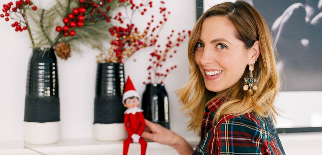 Eva Amurri Martino wears a plaid shirt and puts the Elf On The Shelf on the mantel in her kitchen