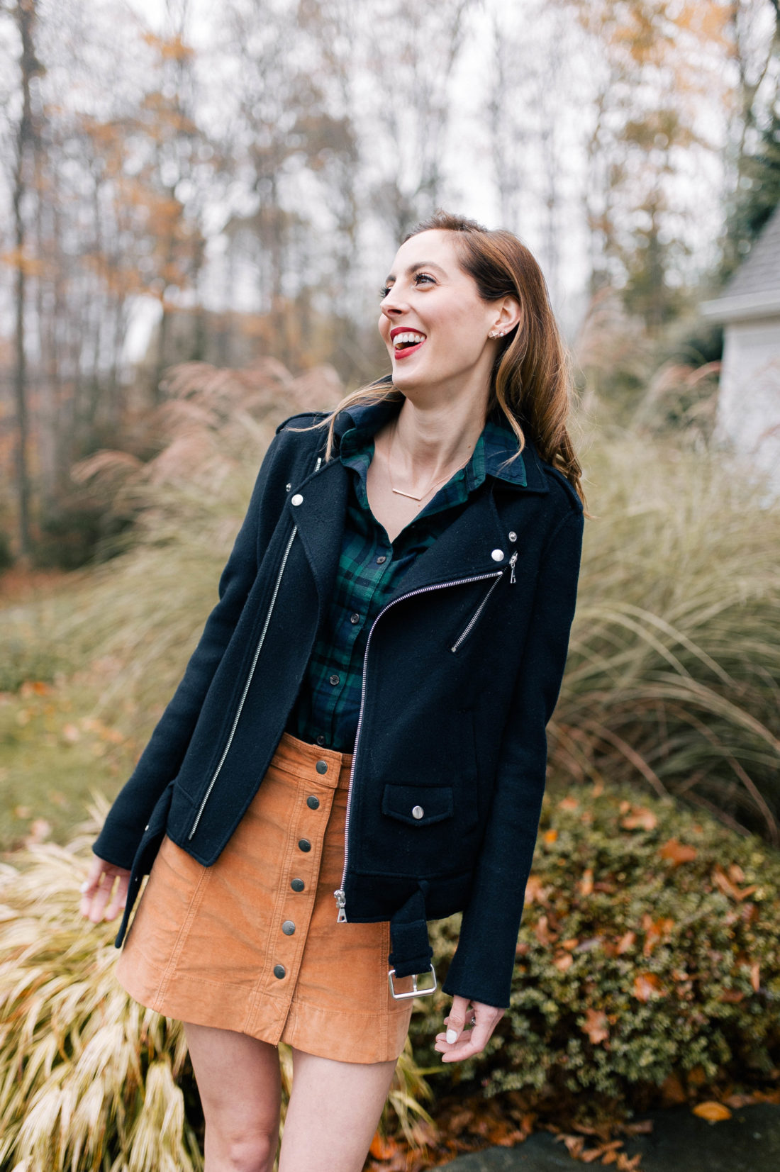 Eva Amurri Martino wears a plaid shirt, velvet button skirt, and blue motorcycle jacket on the pathway outside her Connecticut home