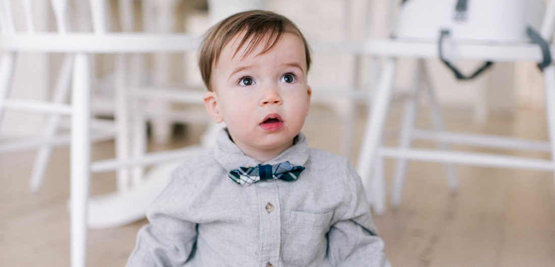 Major Martino wears a grey flannel button down shirt and tartan bow tie, and sits on the kitchen floor in his Connecticut home