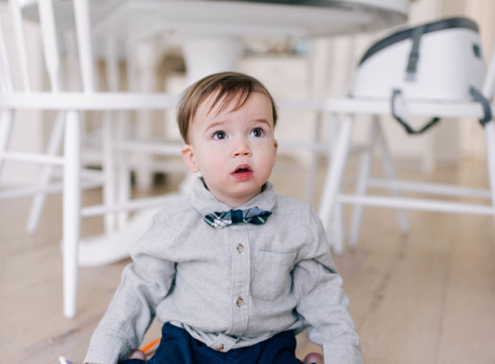 Major Martino wears a grey flannel button down shirt and tartan bow tie, and sits on the kitchen floor in his Connecticut home