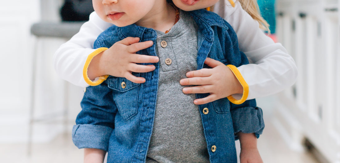 Stylish tot, Major Martino, wears a trendy denim button up over a grey t-shirt, while he gets a hug from older sister Marlowe.
