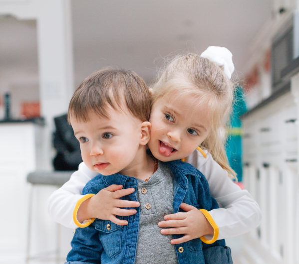 Stylish tot, Major Martino, wears a trendy denim button up over a grey t-shirt, while he gets a hug from older sister Marlowe.