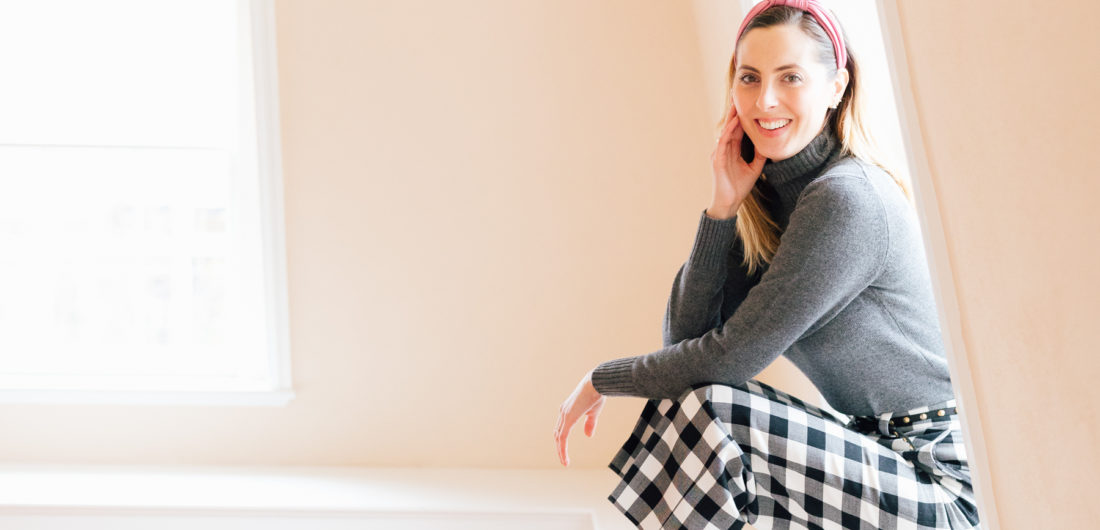 Eva Amurri Martino wears checked trousers and a grey cashmere sweater, and sits in her empty home that awaits renovations
