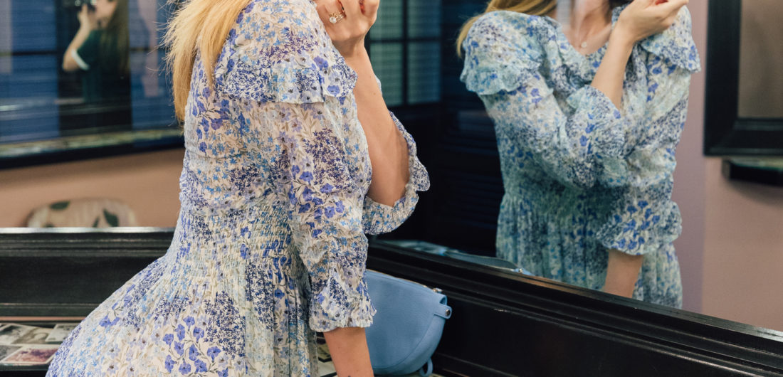 Eva Amurri Martino wears a flowery blue dress and applies lipstick in the mirror at the Claremont Hotel in Atlanta