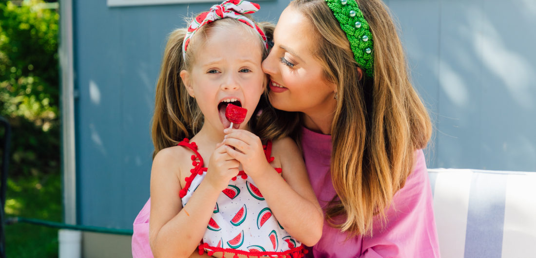 Marlowe Martino sits on mom Eva Amurri Martino's lap eating a watermelon lollipop